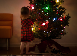 Child placing ornament on a lighted Christmas tree