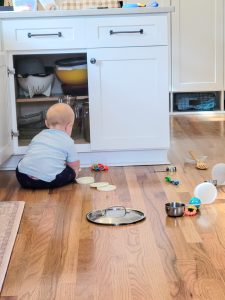Baby sitting in front of kitchen cabinet removing pots and pans